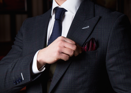 Man adjusting a dark suit jacket with pocket square — Leven’s Clothing
