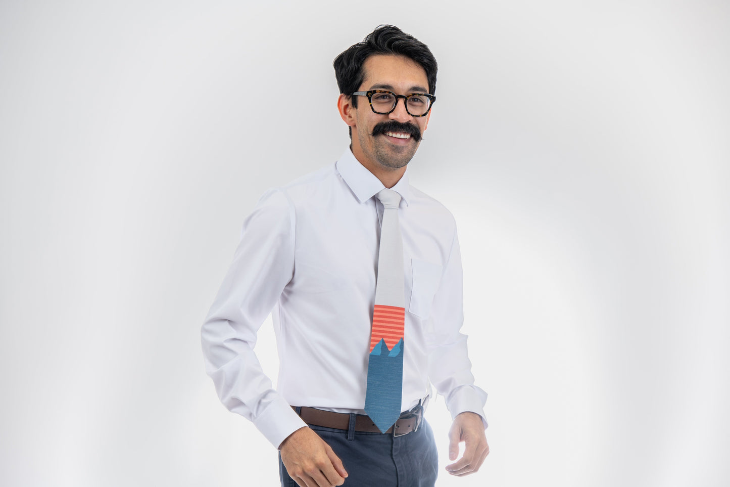 A man wearing a light gray and blue mountain tie with orange and pink. Everyday tie from Kator Shop — versatile Utah menswear piece blending comfort, simplicity, and class.stripes